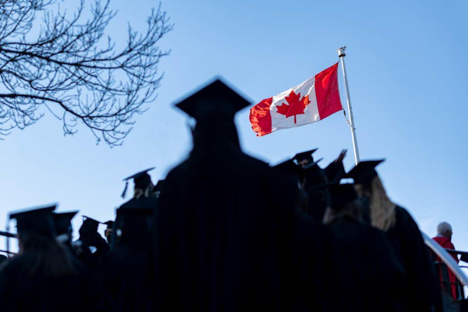 A silhouette of students on graduation day with the Canadian flag in the background
