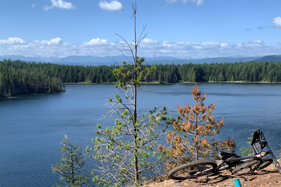 Photo of Quadra lake with trees in background and a bike lying on the ground in the center at the top of a mountain