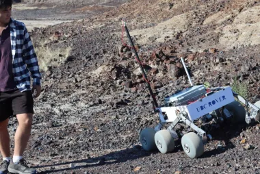 Rover team member walking alongside prototype on a rocky hillsie