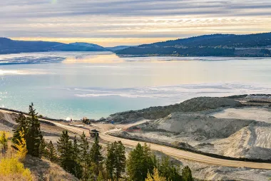 A large body of water, with mountains and sky in the background, and a mine access road and work trucks in the foreground.