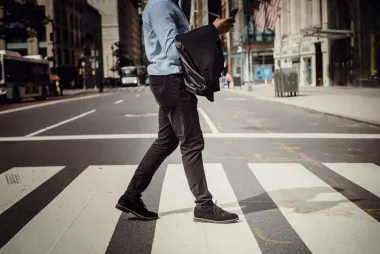 A man crosses a street while looking at his phone.