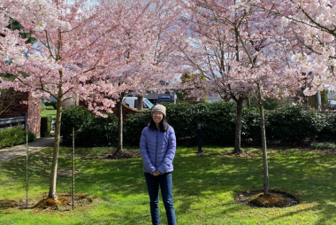 Kira, smiling and standing in front of cherry blossoms