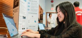 A female student typing on her laptop at a Design and Innovation Day booth