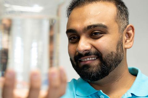 Close-up of Dr. Haroon Mian holding a beaker of clear liquid in front of him