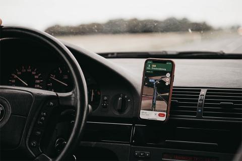 Smartphone turned-on in vehicle mount inside vehicle with black steering wheel on the left.