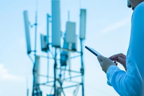 Communication tower in the background with a person with a phone in the front.