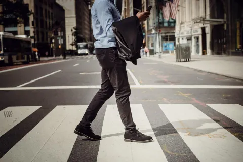 A man crosses a street while looking at his phone.