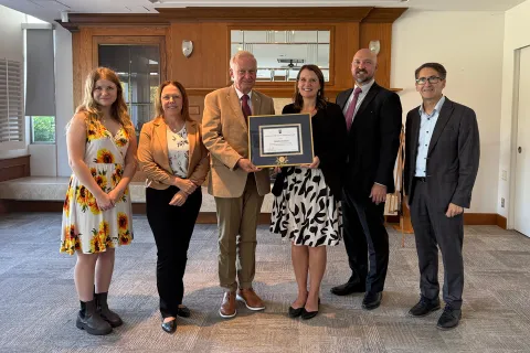 Jim McEwen presents Heather Eckton with a framed certificate, accompanied by Jim's children, Jordan Dearsley and Dean James Olson. 