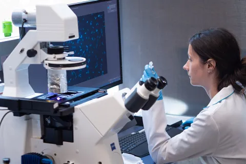 A person in a lab coat sitting at a large microscope