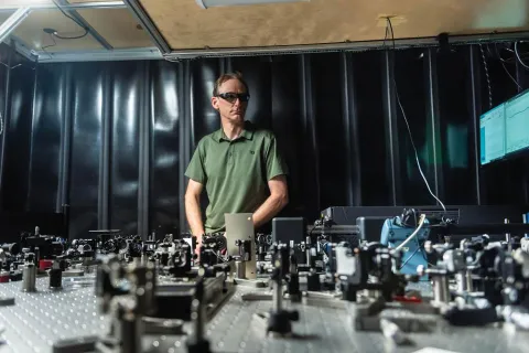 A man wearing sunglasses stands with an array of equipment