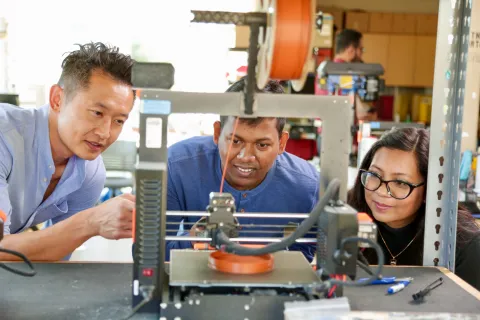 Three people watching a 3D printer