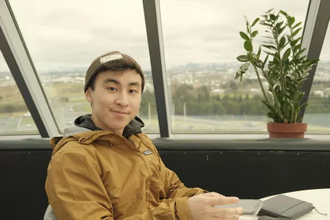 UBC Engineering grad Michael Ko smiles for the camera while sitting next to a window overlooking a view from Iceland