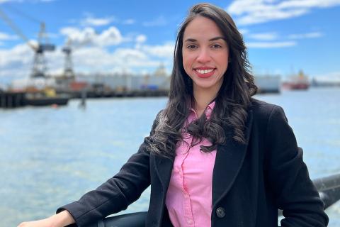 Paloma Chagas Guerra Pereira smiles for the camera while positioned centre in front of a body of water near a port with machinery in the distance