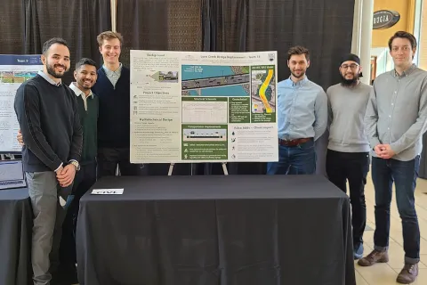 Team members smiling as they present their project poster at the Design and Innovation Day
