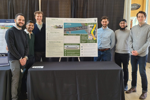 Team members smiling as they present their project poster at the Design and Innovation Day 