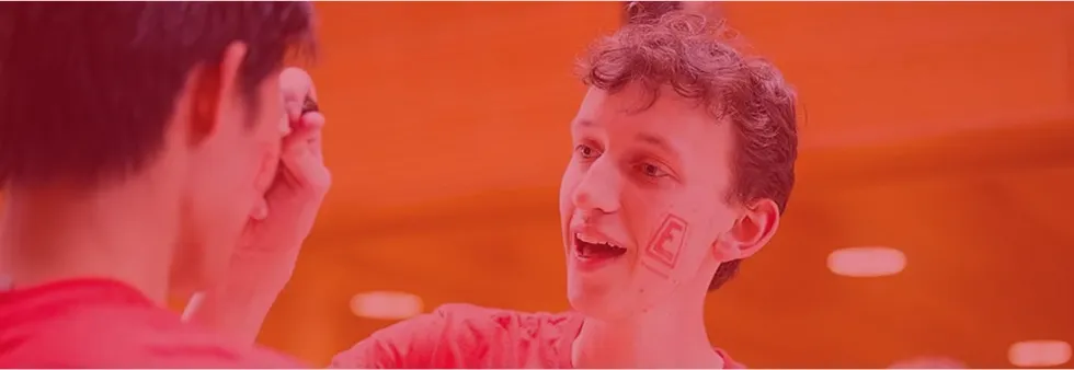 An engineering student with a temporary E tatoo on his face interacting with another student.