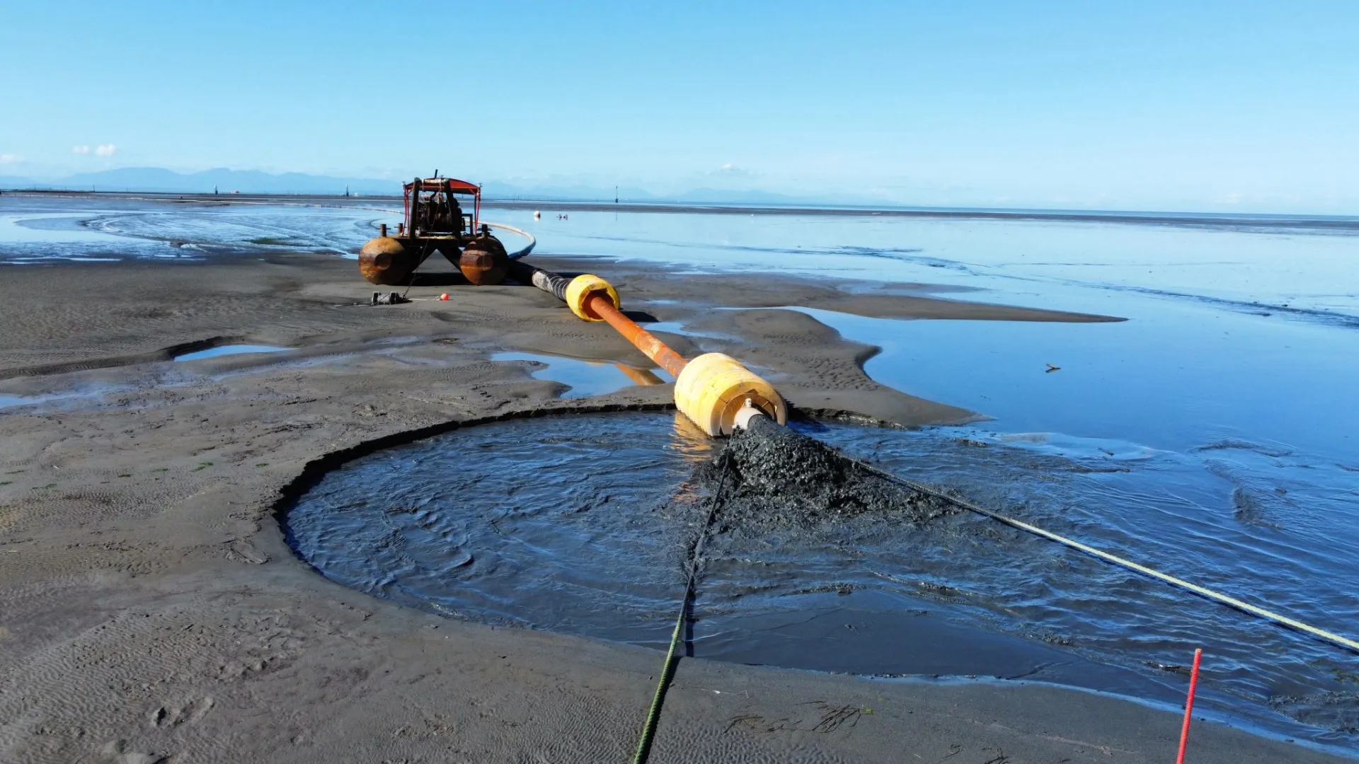 A pipe for depositing sediment sits in shallow water